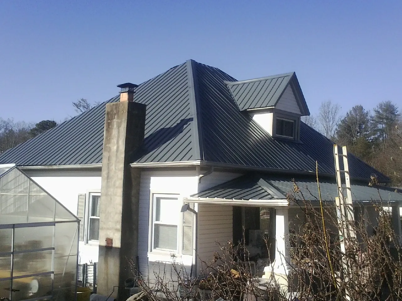 Dark blue standing seam metal roof on a white farmhouse with dormer — Slate & Tile Roof Repair by Roofing Brothers in Winchendon