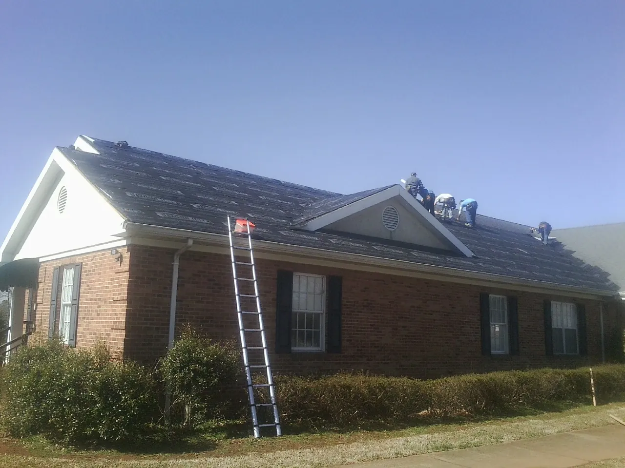 Crew tearing shingles off a brick ranch roof with a ladder set — Metal Roof Repair work by our crew in Winchendon