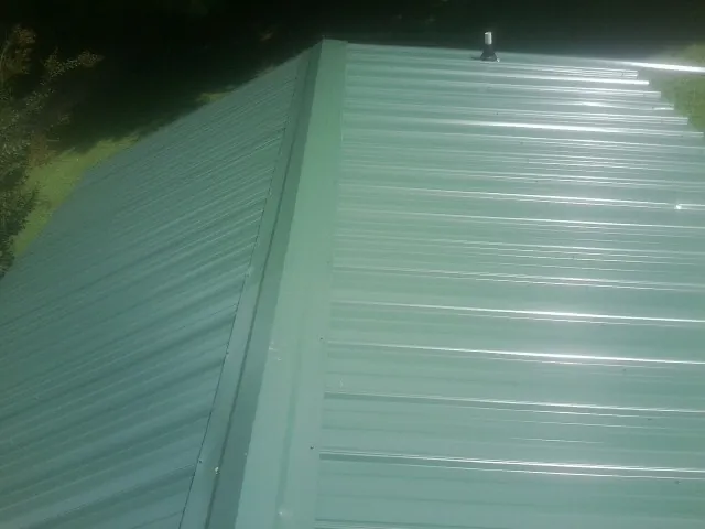 New green metal panels meeting at the ridge of a roof — Flat Roof Repair work by our crew in Winchendon