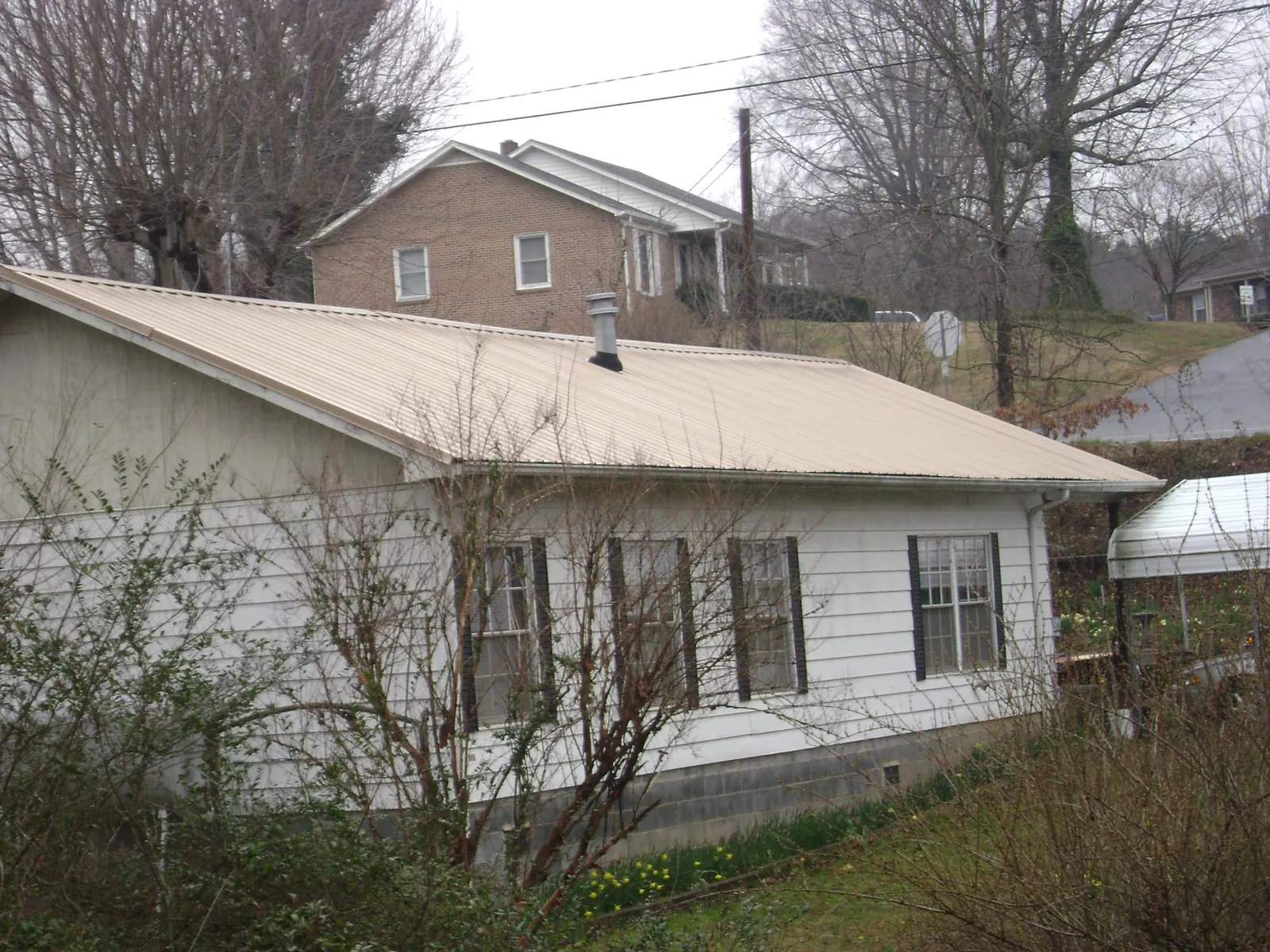 Tan metal roof on a white sided house set into a hillside — Commercial Roofing by Roofing Brothers in Winchendon